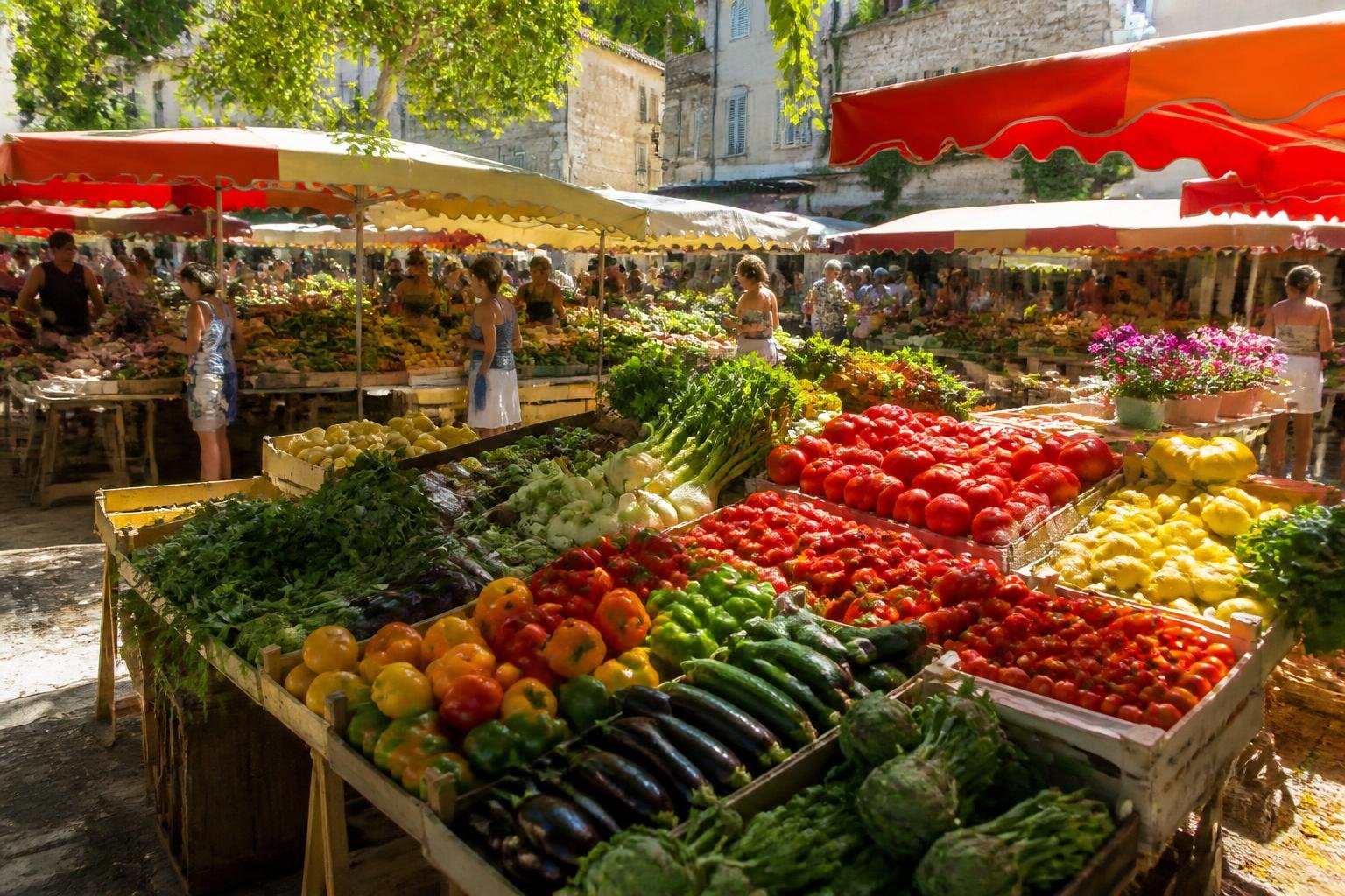 Vue d'ensemble d'un marché provençal avec étals débordant de légumes et fruits colorés sous le soleil
