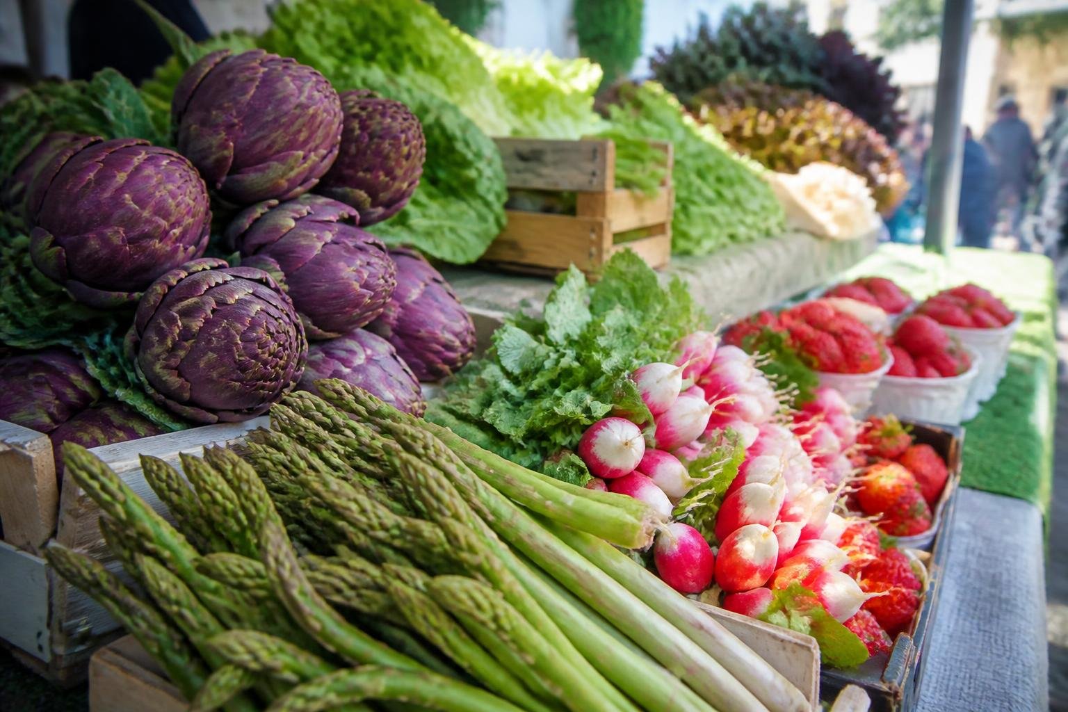 Étals de marché printanier avec artichauts violets, asperges vertes et radis croquants